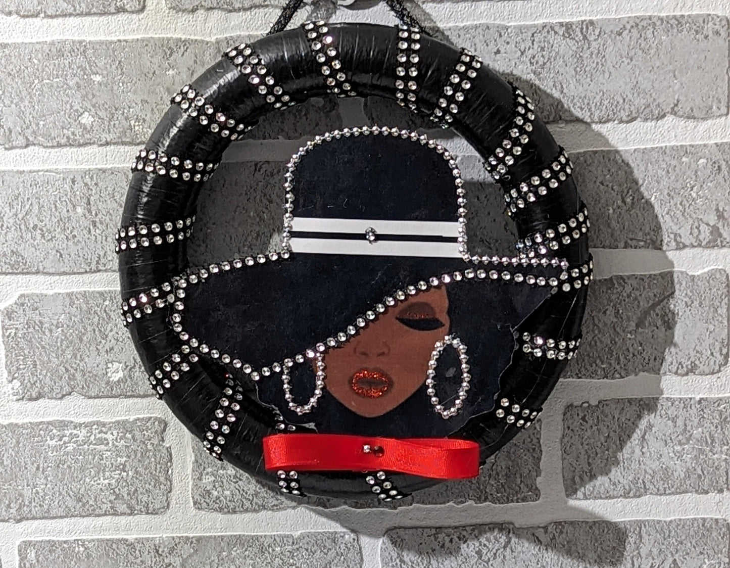 Decorative Lady Black Wreath with a stylized face design on a stand, featuring black hair, red ribbon, and silver embellishments.