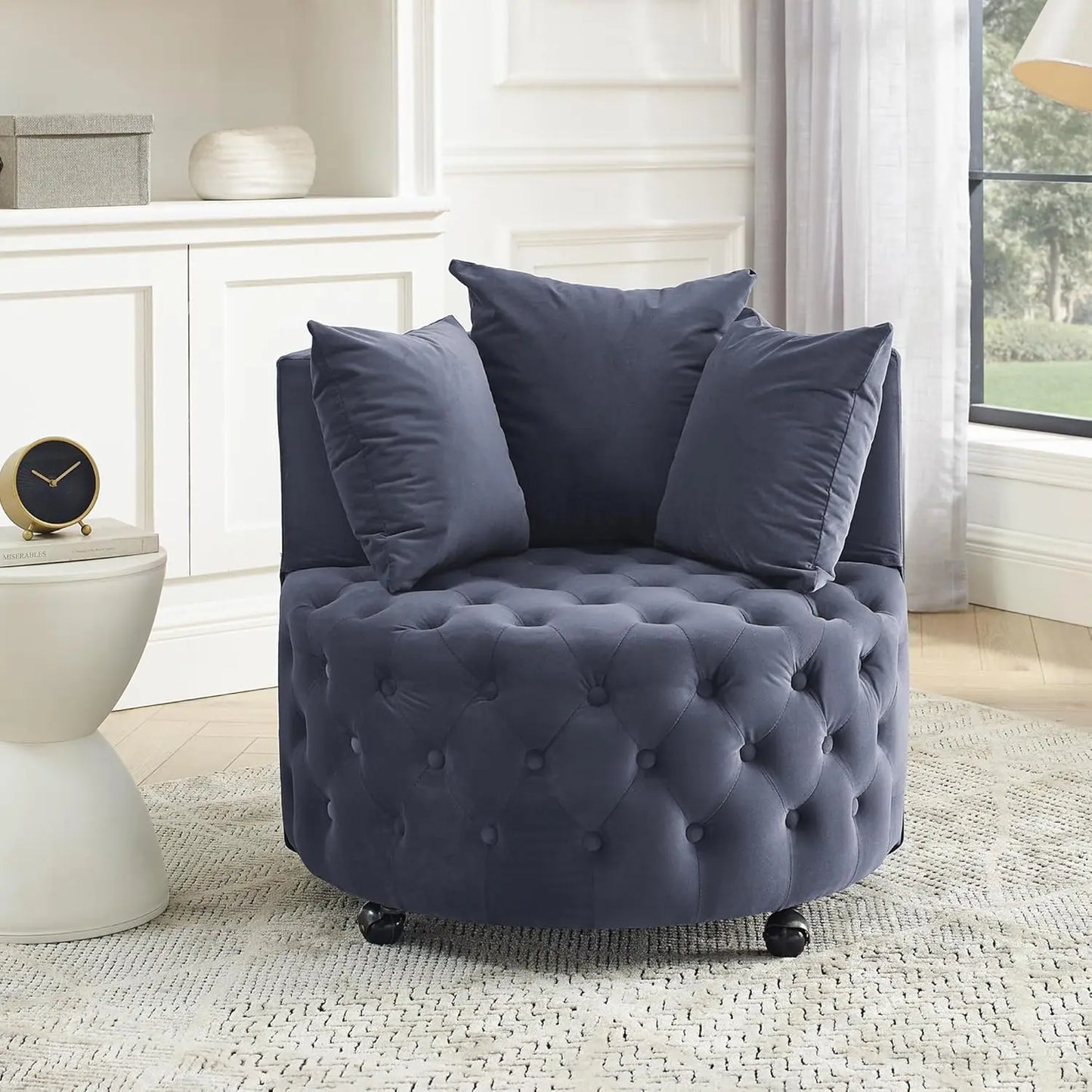 Blue tufted armchair with three pillows in a room with a white cabinet and window.