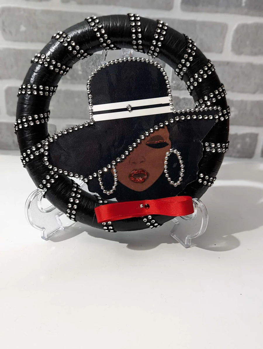 Decorative Lady Black Wreath with a stylized face design on a stand, featuring black hair, red ribbon, and silver embellishments.