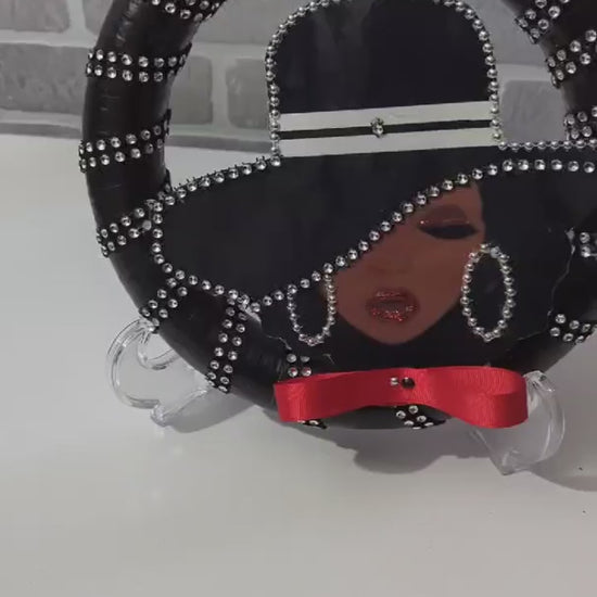 Decorative Lady Black Wreath with a stylized face design on a stand, featuring black hair, red ribbon, and silver embellishments.